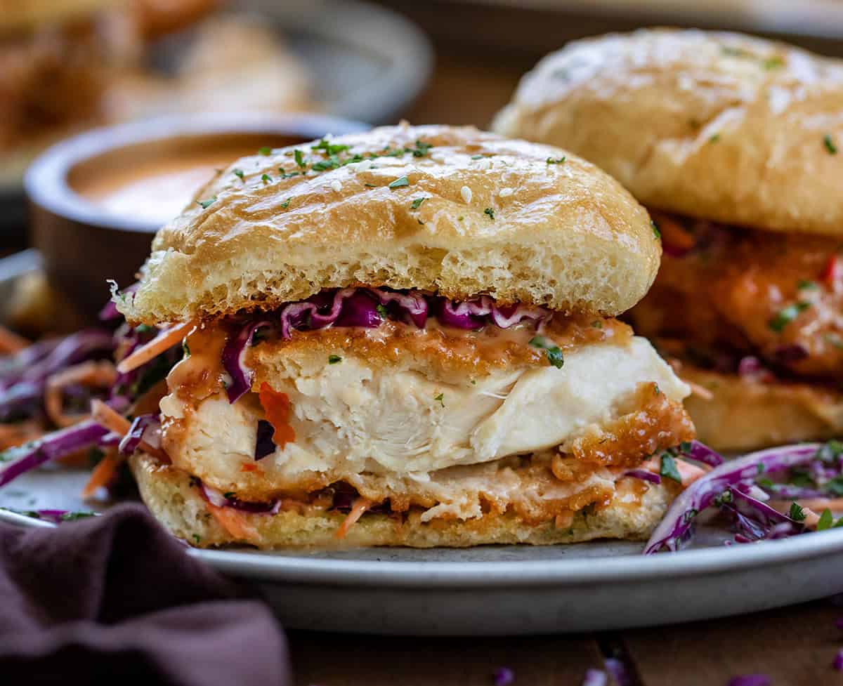 Bang Bang Chicken Sandwich with crispy chicken covered in Bang Bang Sauce and topped with slaw close up and cut in half to show tender chicken.