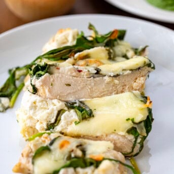 Sliced chicken covered in cheese and spinach on a white plate.