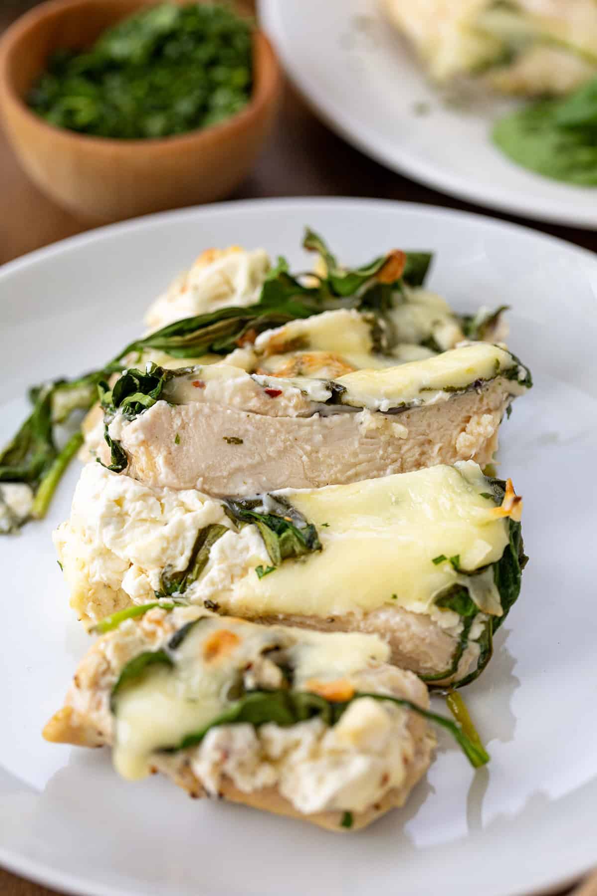 Sliced chicken covered in cheese and spinach on a white plate.