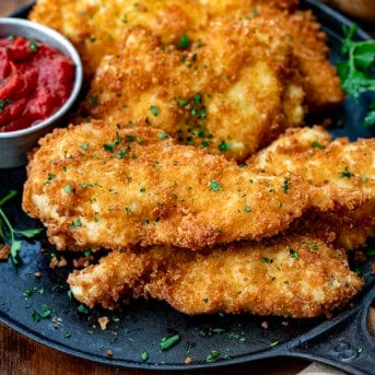 Easy Chicken Cutlets on a black skillet with marinara sauce.