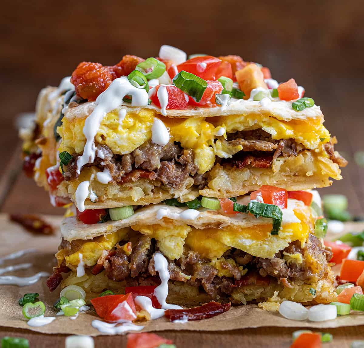 Pieces of a breakfast wrap stacked on itself and showing inside layers of hash brown, egg, bacon, sausage, and tomatoes.