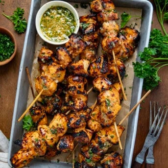 Honey Garlic Chicken Skewers in a tray with butter sauce on a wooden table from overhead.