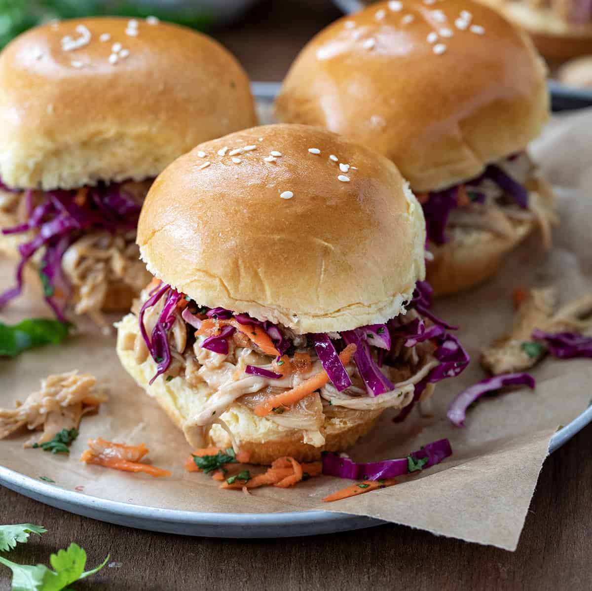 Three Honey Garlic Chicken Sliders on a plate on a wooden table. 