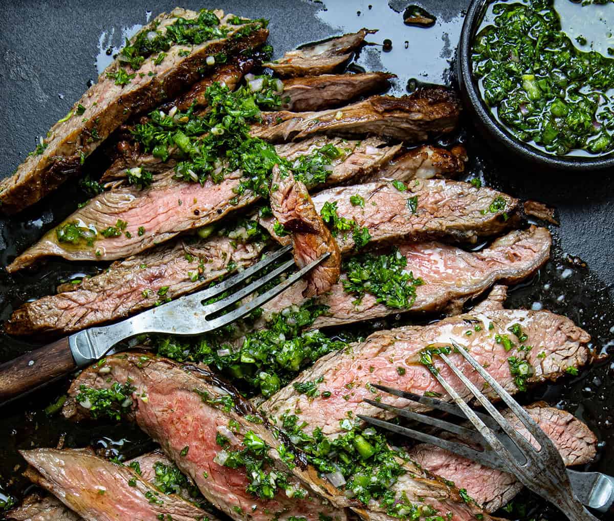 Chimichurri London Broil cut into strips showing tender medium-rare beef covered in chimichurri sauce.