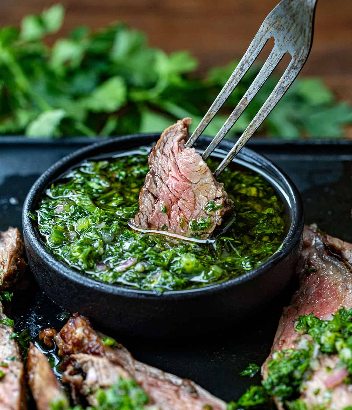 Fork dipping a piece of steak into chimichurri sauce.