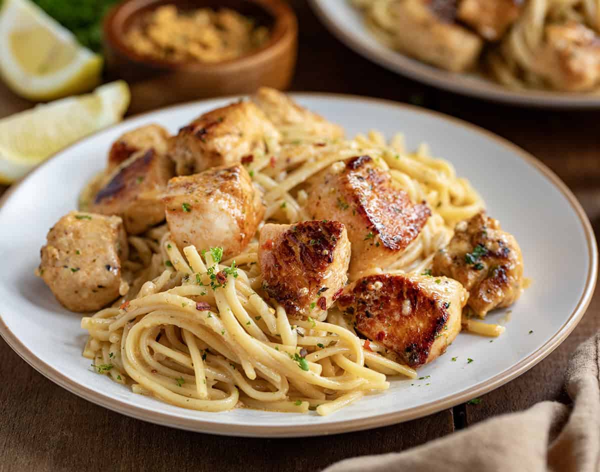 Plate of cowboy butter coated pasta with chicken bites on a wooden table.