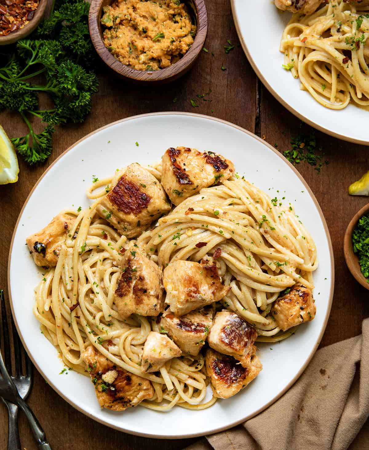 Plates of Cowboy Butter Chicken Linguine on a wooden table with cowboy butter and fresh lemon wedges from overhead.