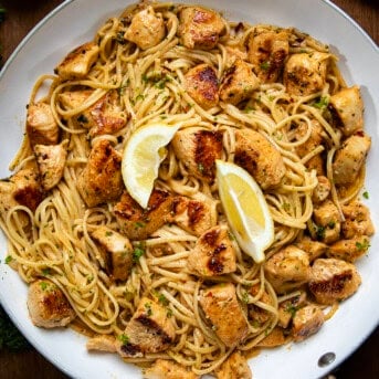 Cowboy Butter Chicken Linguine in a white skillet with lemon wedges from overhead.
