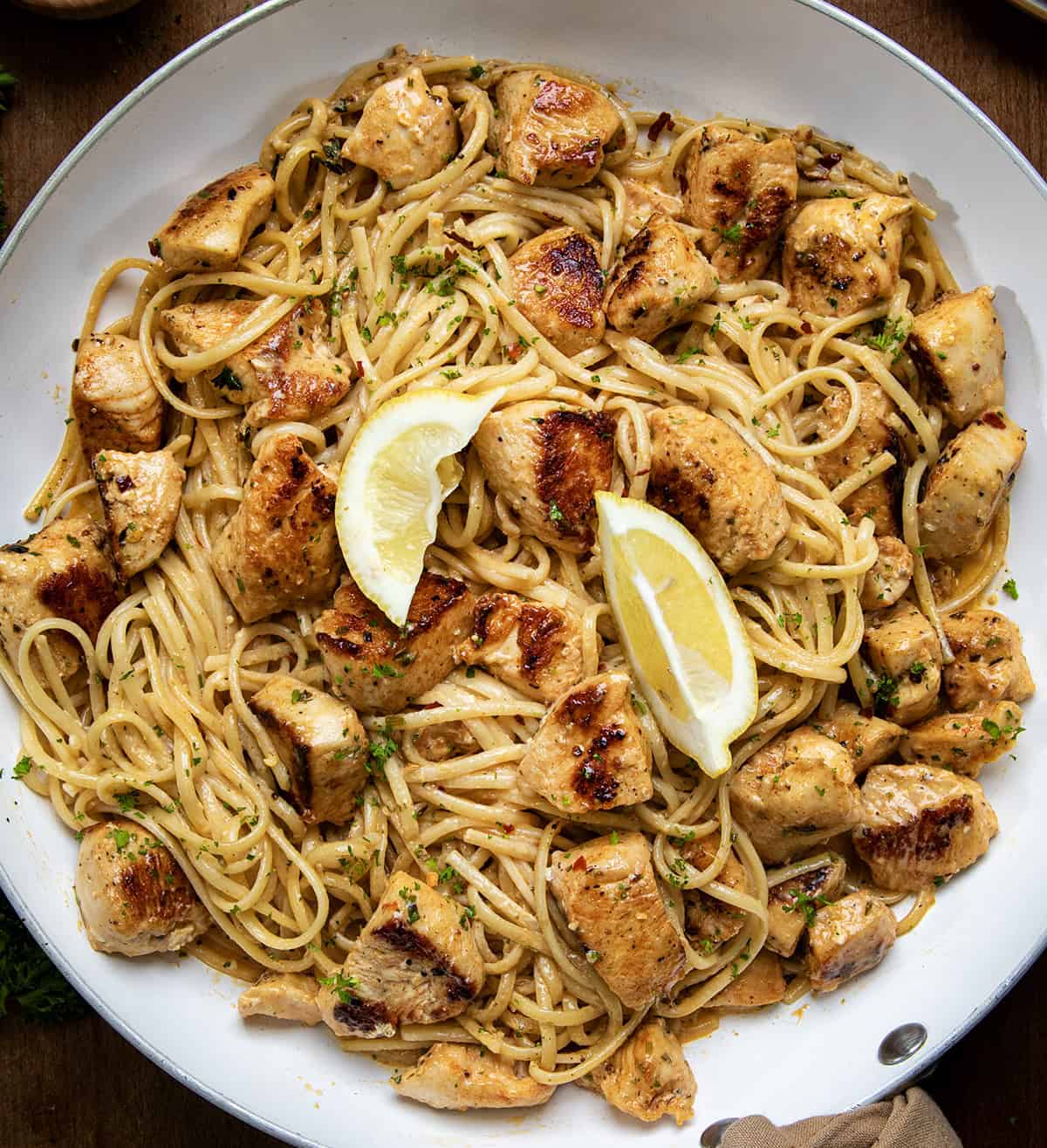 Cowboy Butter Chicken Linguine in a white skillet with lemon wedges from overhead.