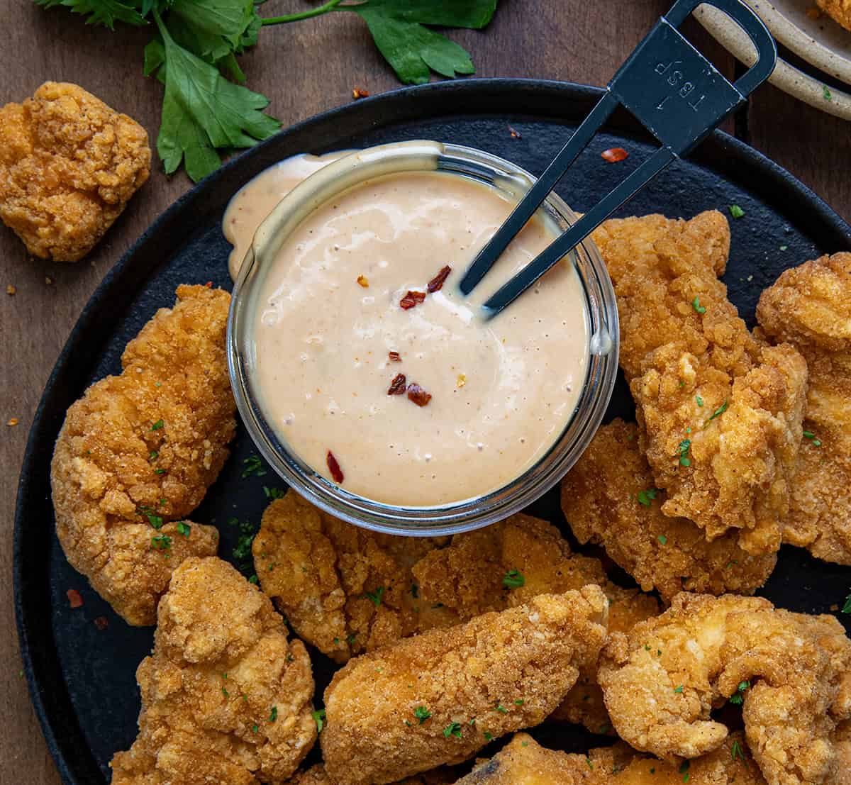 Jar of Creamy Honey Mustard Sauce on a plate filled with crispy chicken tenders.