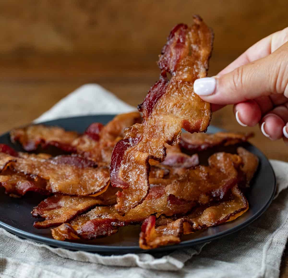 Hand Holding Piece of Bacon.