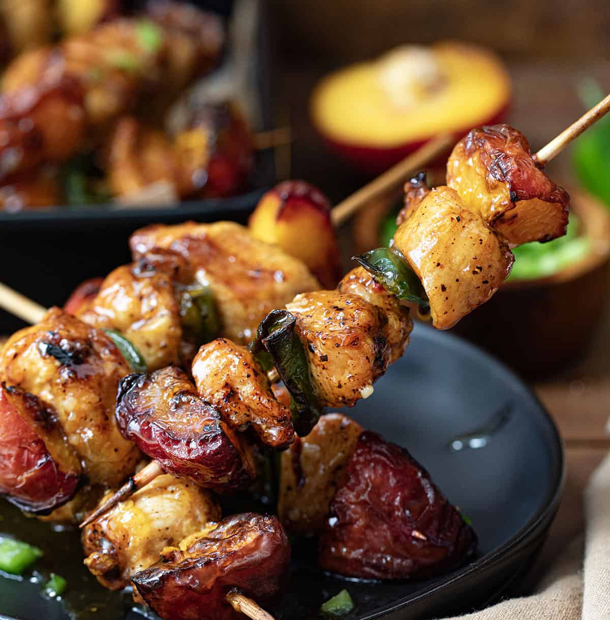 Holding up one Jalapeno Peach Chicken Skewers in front of others on a black plate on a wooden table.