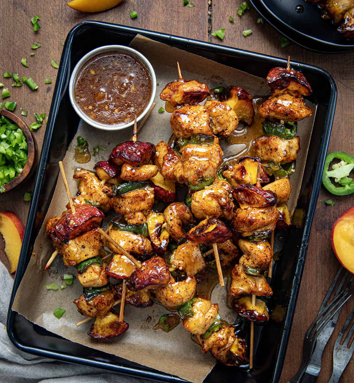 Jalapeno Peach Chicken Skewers in a tray on a wooden table surrounded by fresh peaches and diced jalapeno from overhead.