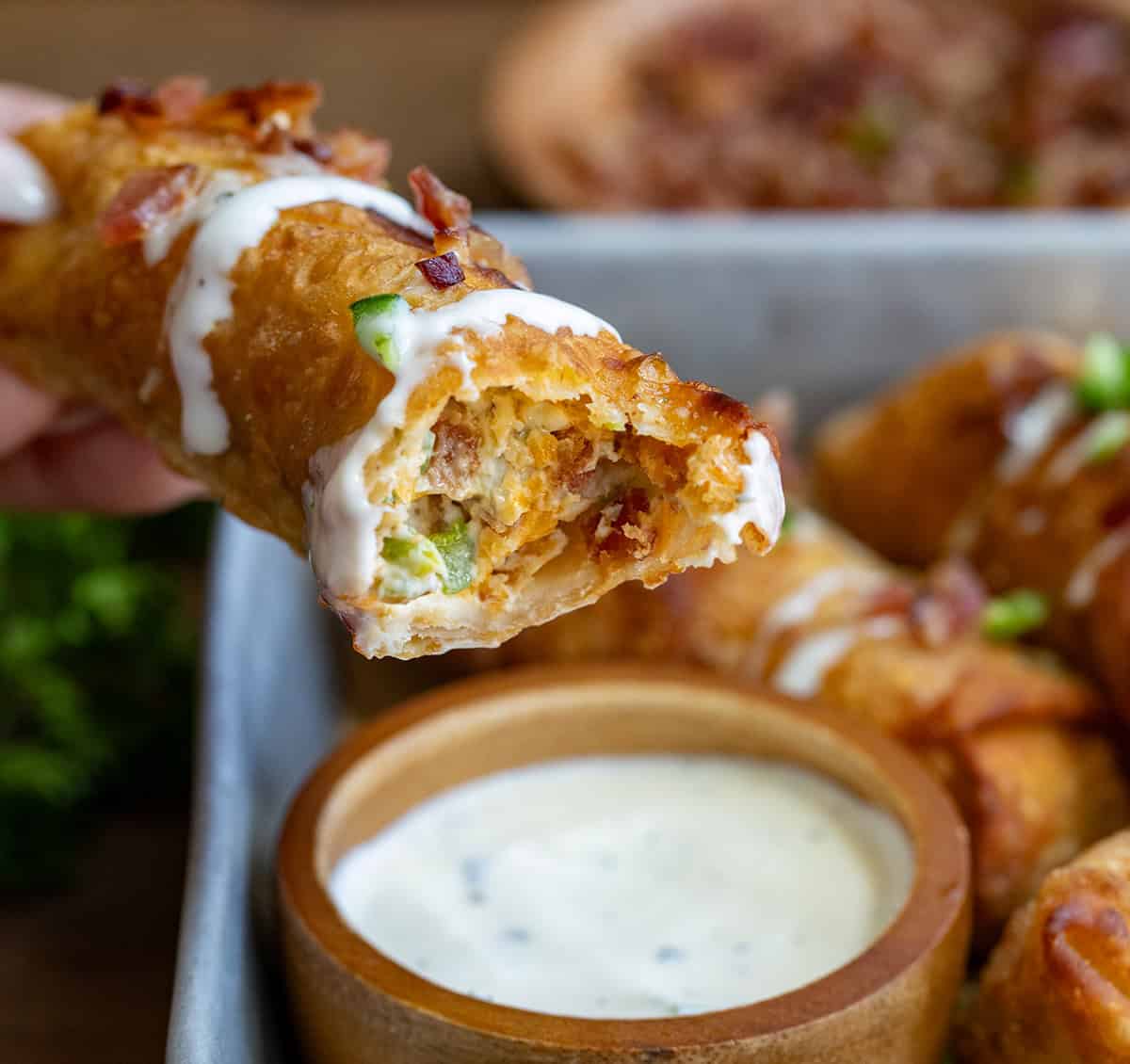 A bit into Jalapeno Popper Egg Roll that has been dipped into ranch and shows the creamy filling.