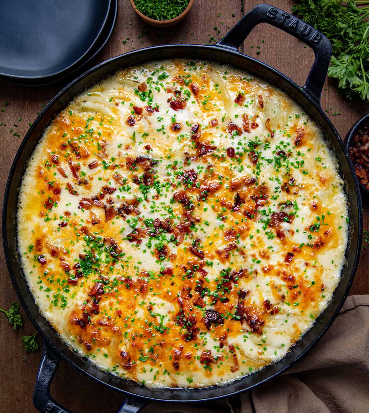 Skillet of Loaded Scalloped Potatoes on a wooden table from overhead.