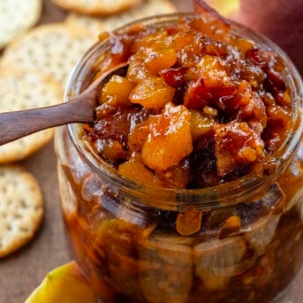 Jar of Peach Bacon Jam with a mini wooden spoon.