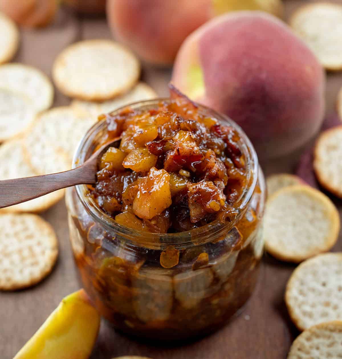 Jar of Peach Bacon Jam with a mini wooden spoon.