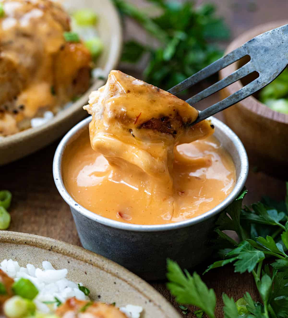 Dipping a piece of chicken into bang bang sauce.