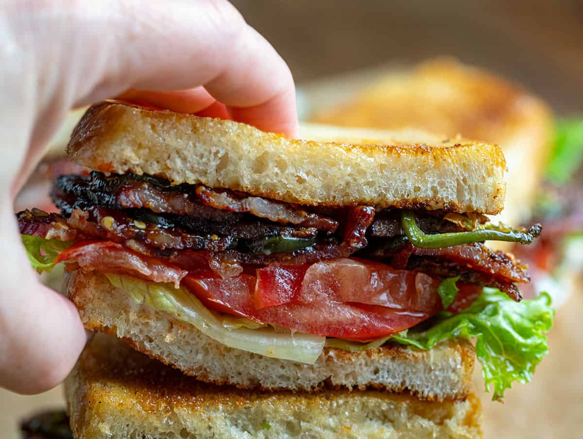 Hand picking up half of a Spicy Candied Bacon BLT.