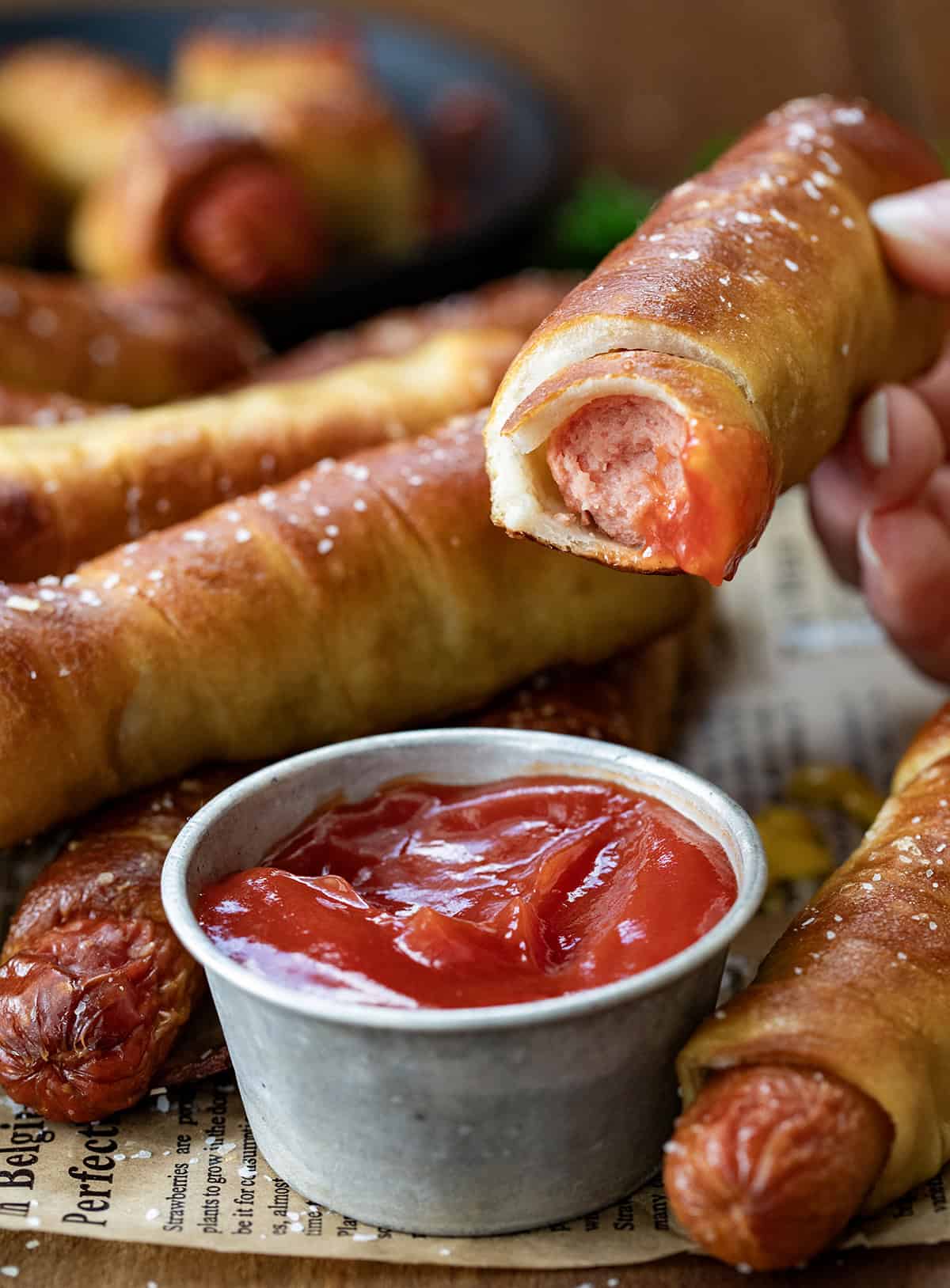 Dipping a Pretzel Dog into ketchup and a bite taken out of it.