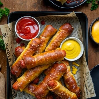 Pretzel Dogs in a pan with ketchup and mustard on a wooden table from overhead.