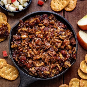 Mini Skillet of Apple Whiskey Bacon Jam surrounded by crackers and diced apples.