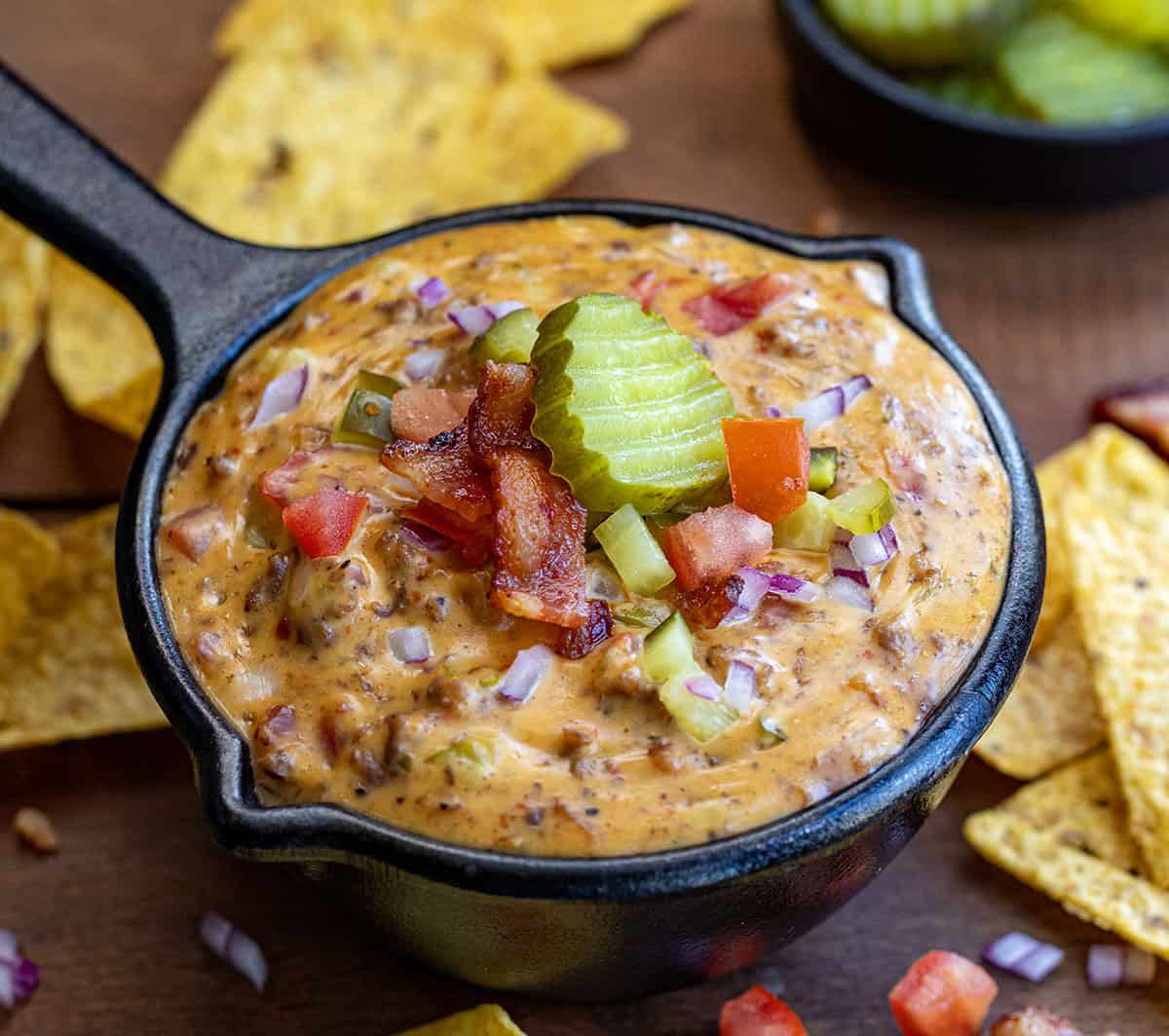 Mini skillet of Cheeseburger Dip on a wooden table surrounded by chips.