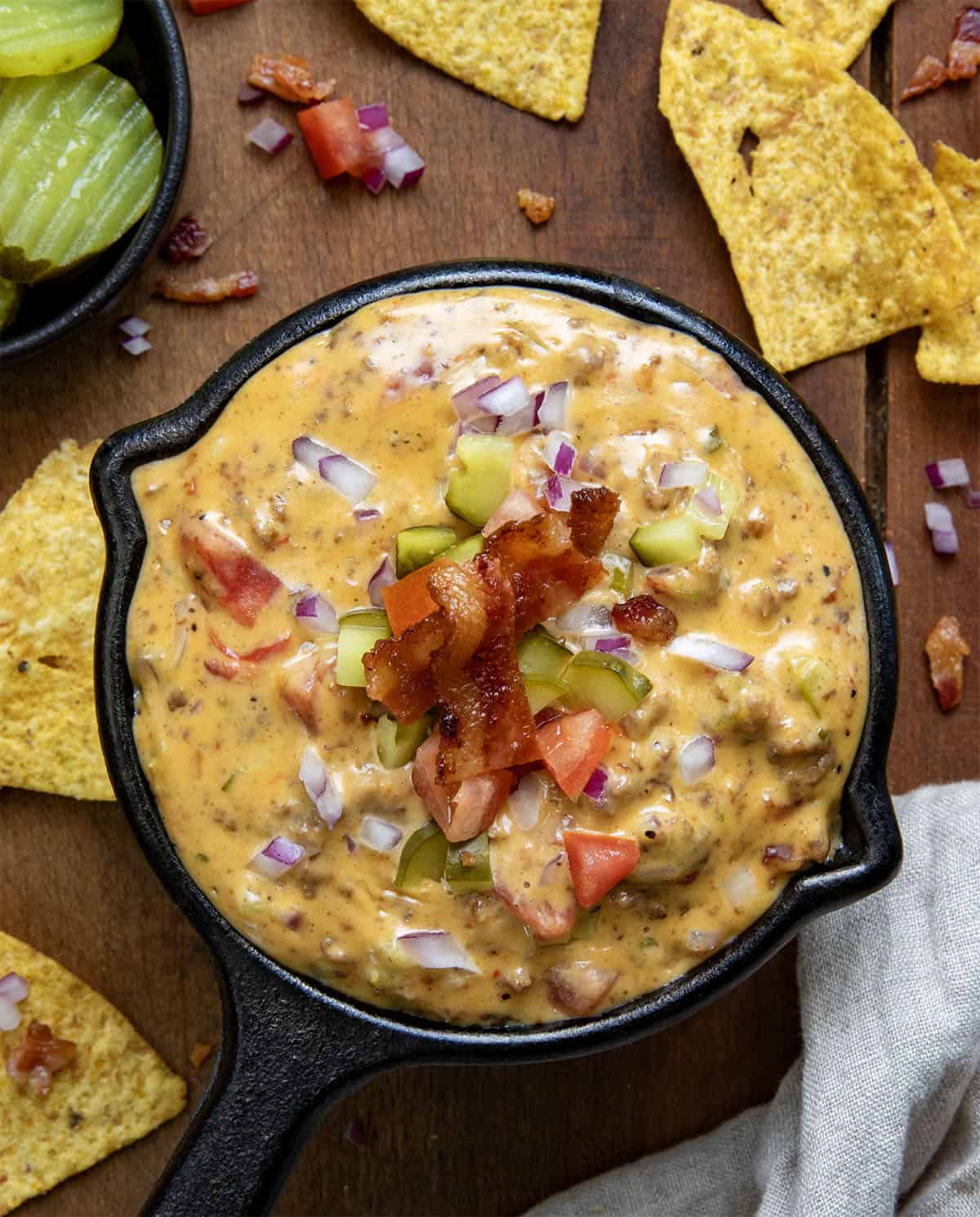 Mini skillet of Cheeseburger Dip on a wooden table surrounded by chips. 