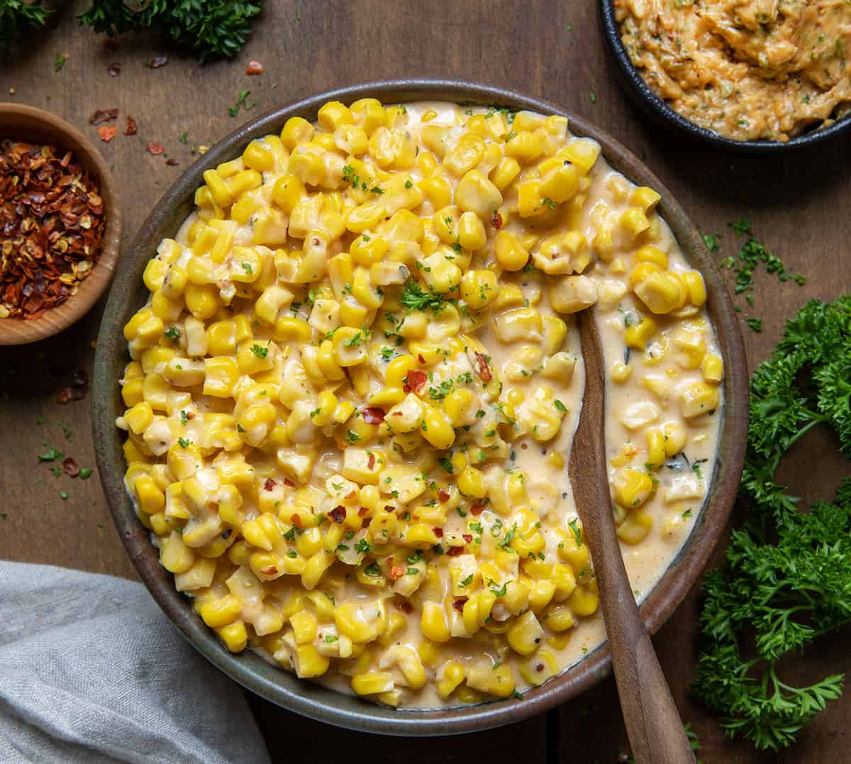 Bowl of Cowboy Butter Creamed Corn on a wooden table with a spoon in it from overhead.