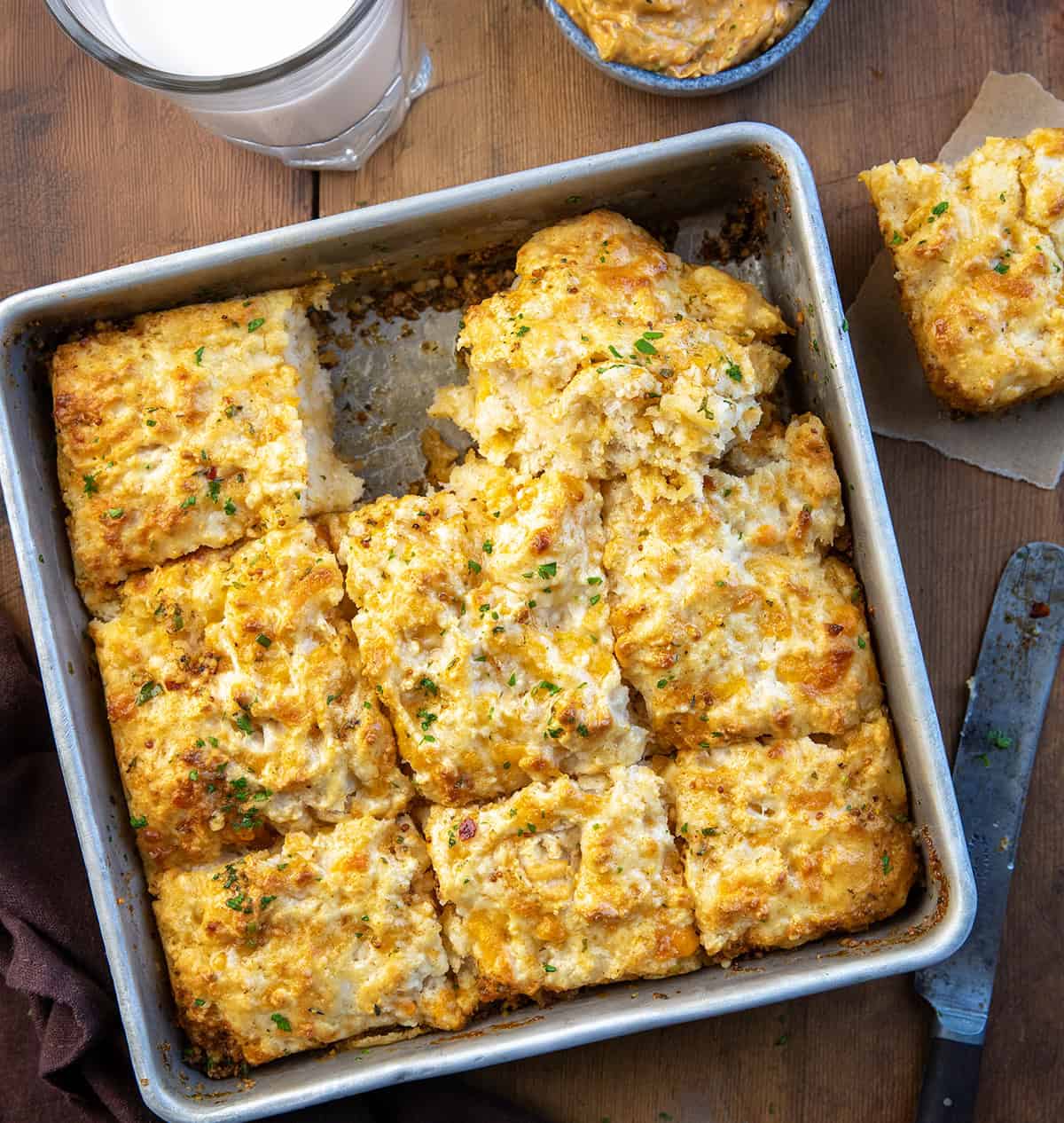 Pan of Cowboy Butter Swim Biscuits with one on a plate and one on its side in the pan.