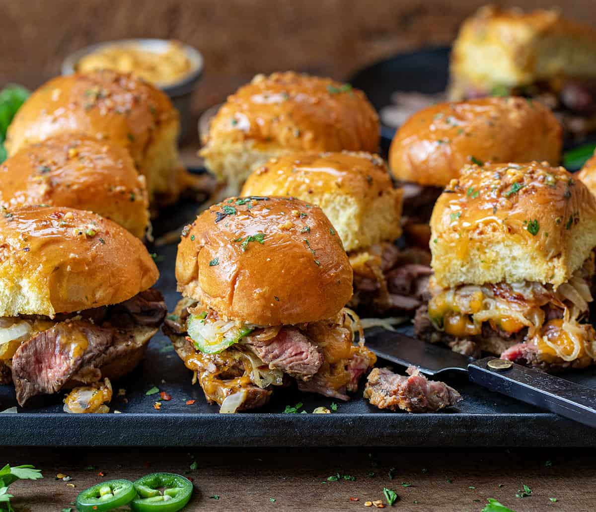 Tray of Cowboy Steak Sliders on wooden table surrounded by fresh jalapeno.