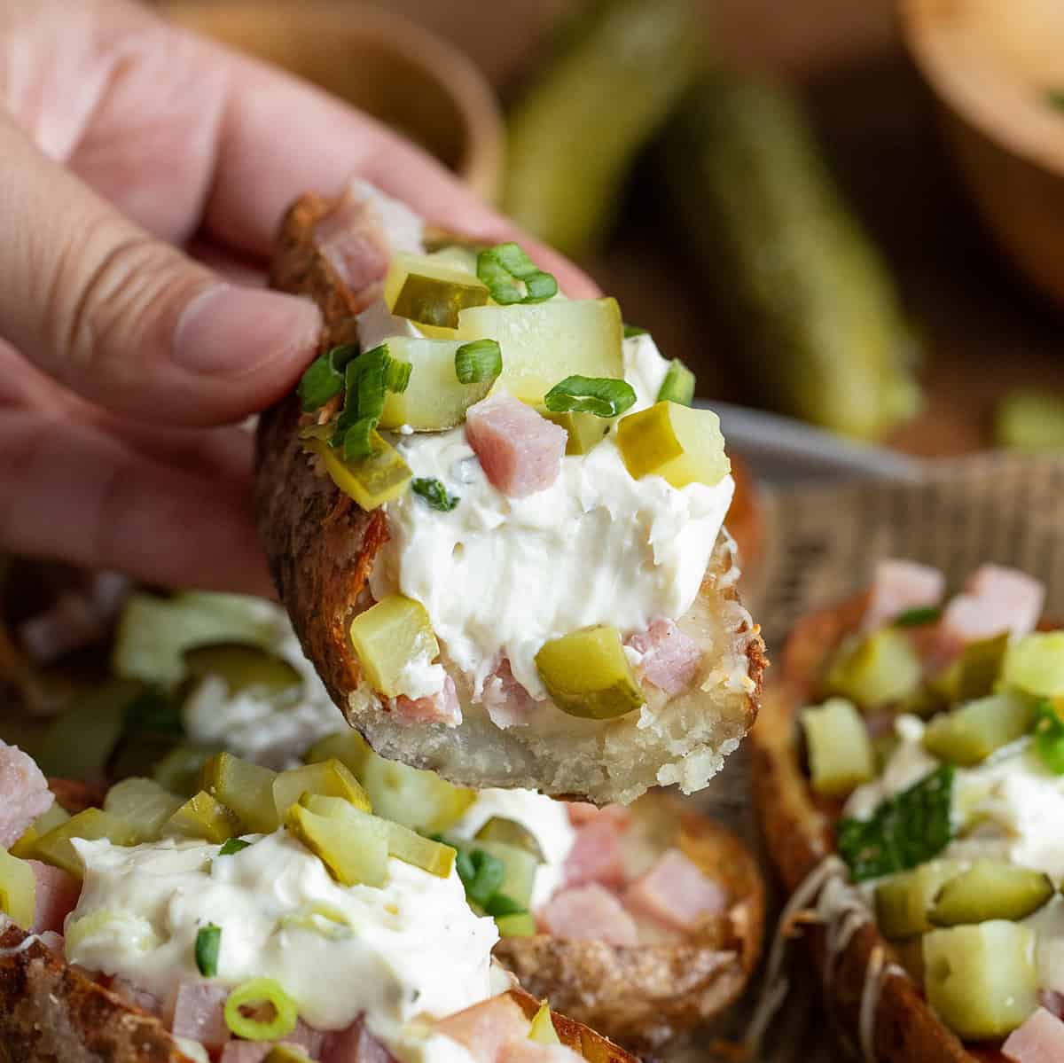 Hand holding a bit into Ham and Pickle Potato Skin.