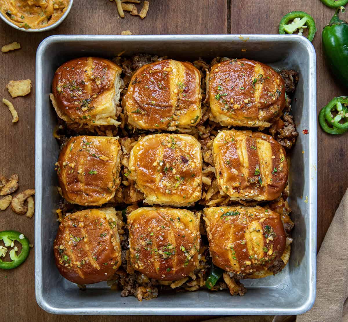 Pan of Pretzel Cowboy Sliders on a wooden table surrounded by fried onions and cowboy butter from overhead.