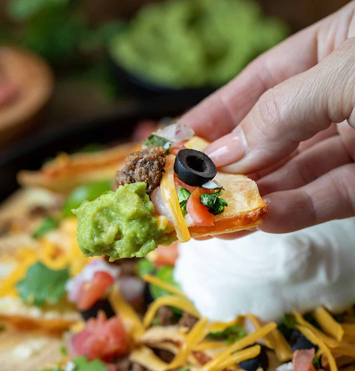 Hand holding a Quesadilla Nacho topped with guacamole, cheese, and and olive.