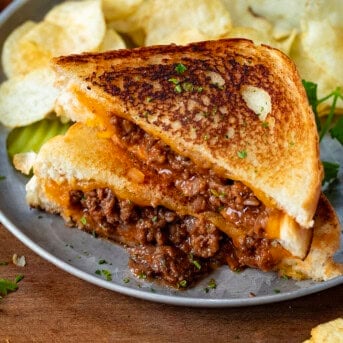 Sloppy Joe Grilled Cheese Sandwich on a plate cut in half and with chips.