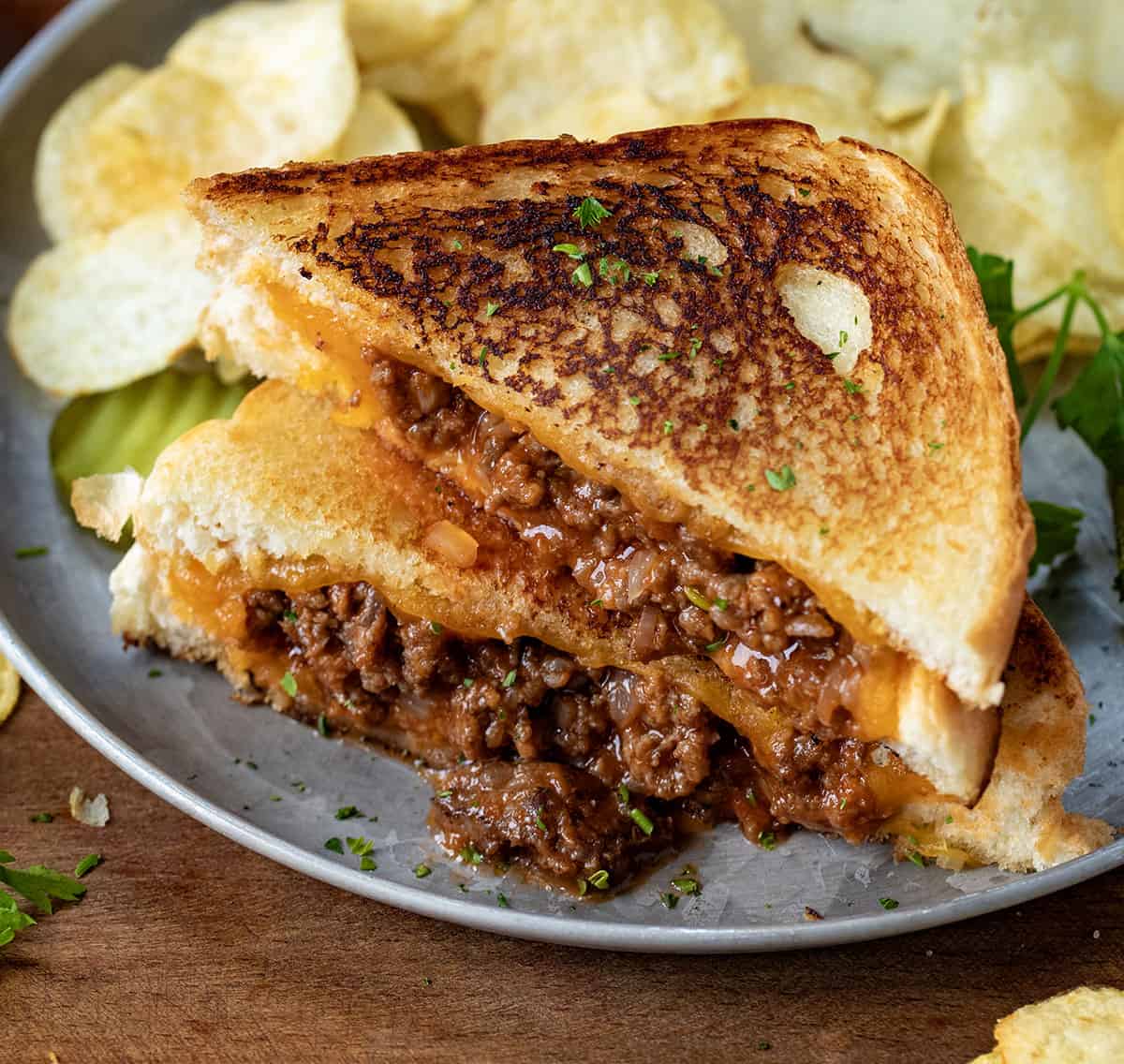 Sloppy Joe Grilled Cheese Sandwich on a plate cut in half and with chips.