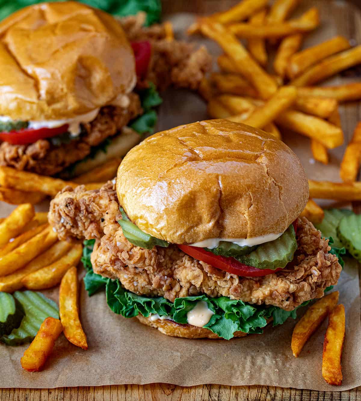 A couple of Spicy Chicken Sandwiches with french fries on a wooden table.