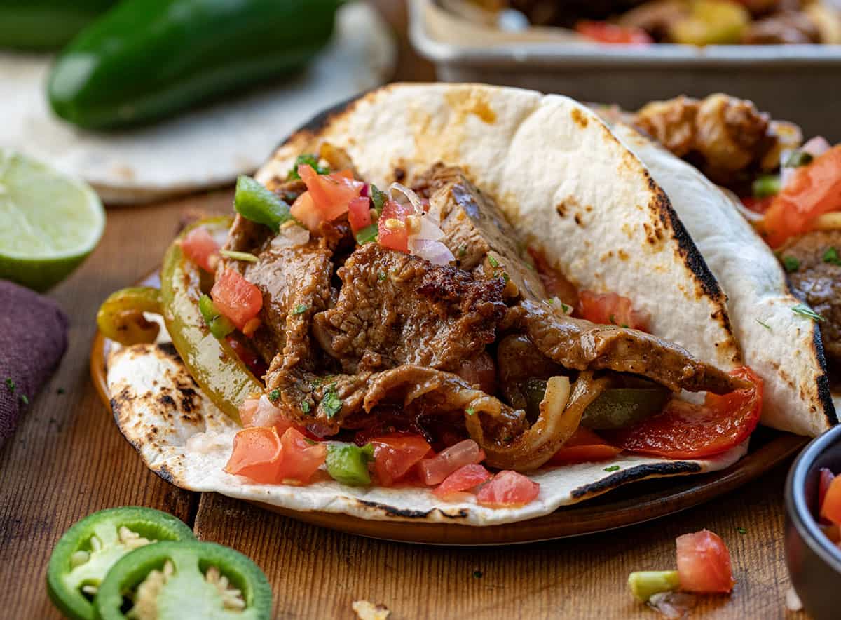 Steak Fajita Taco on a plate on a wooden table with pico on top.