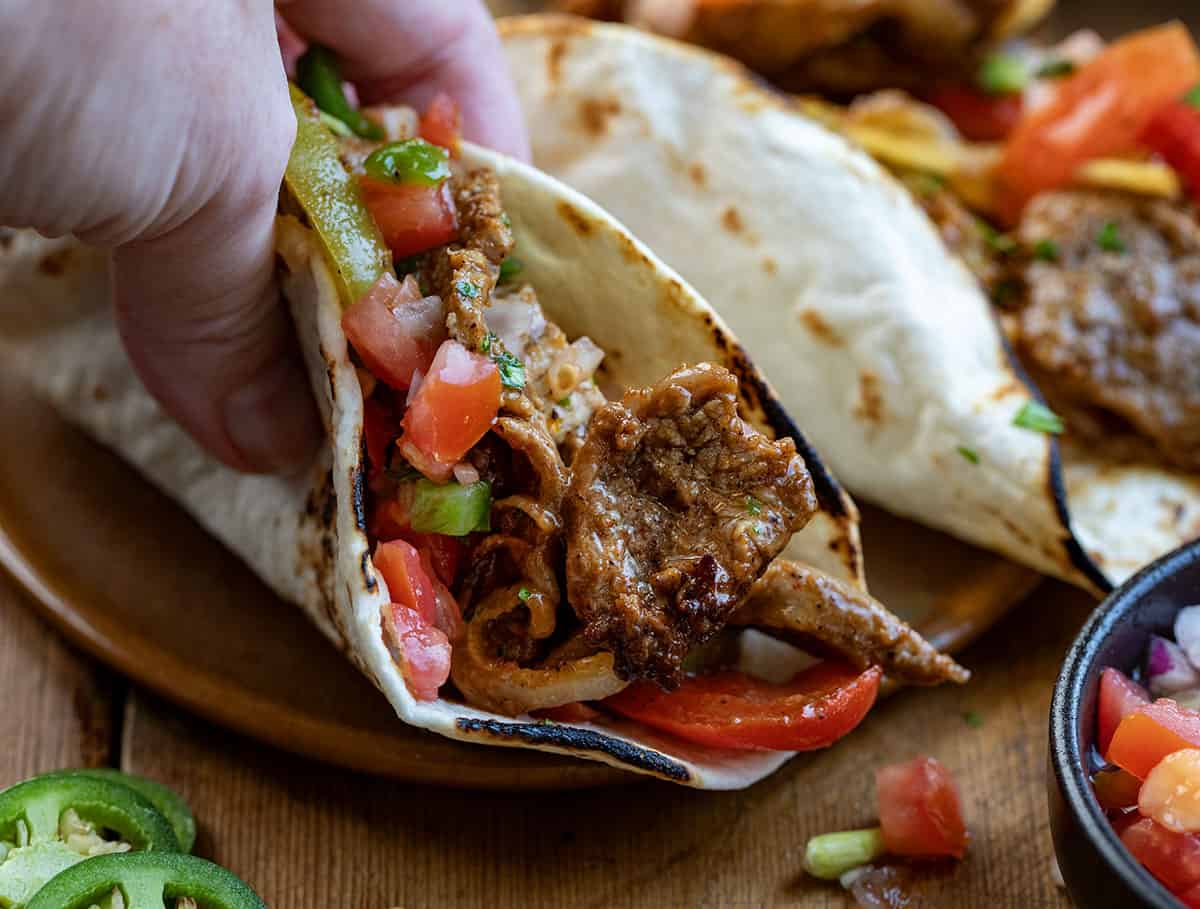 Hand picking up a Steak Fajita taco from a plate.