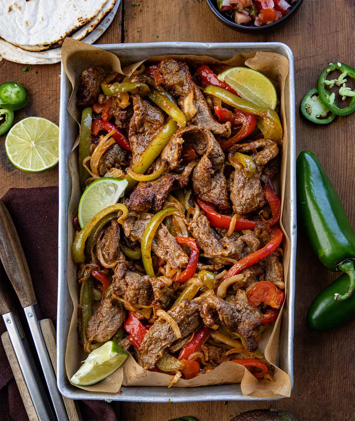 Pan of steak, peppers, and onions on a wooden table from overhead. 