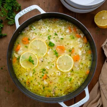 Pot of Lemon Chicken Orzo Soup on a wooden table with fresh lemon from overhead.