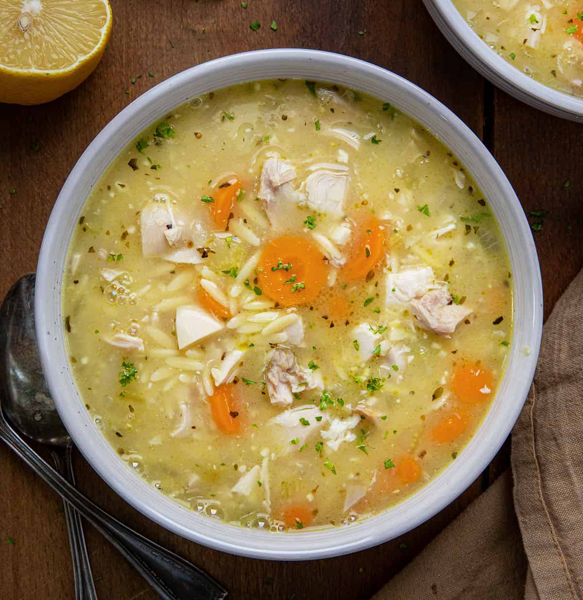 Bowls of Lemon Chicken Orzo Soup on a wooden table from overhead.