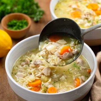 Ladling Lemon Chicken Orzo Soup into a white bowl.