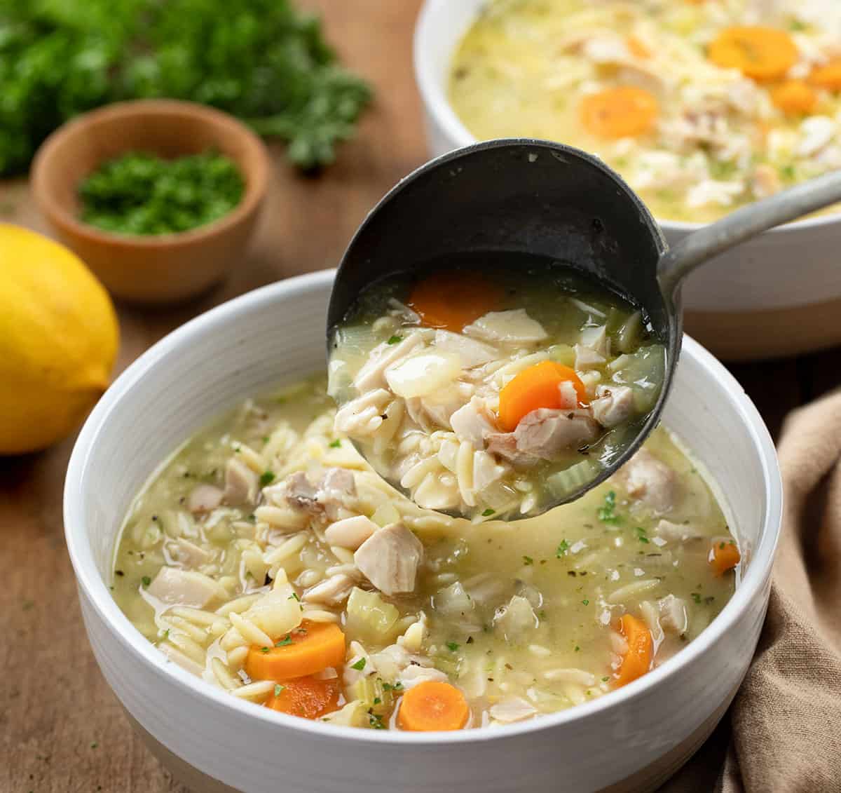 Ladling Lemon Chicken Orzo Soup into a white bowl.