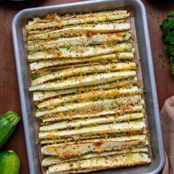 Sheet pan of Baked Zucchini Sticks on a wooden table from overhead.