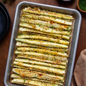 Sheet pan of Baked Zucchini Sticks on a wooden table from overhead.