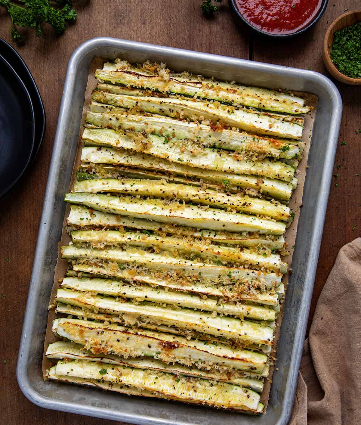 Sheet pan of Baked Zucchini Sticks on a wooden table from overhead.