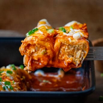 Spatula picking up Buffalo Chicken Enchiladas from the casserole pan.