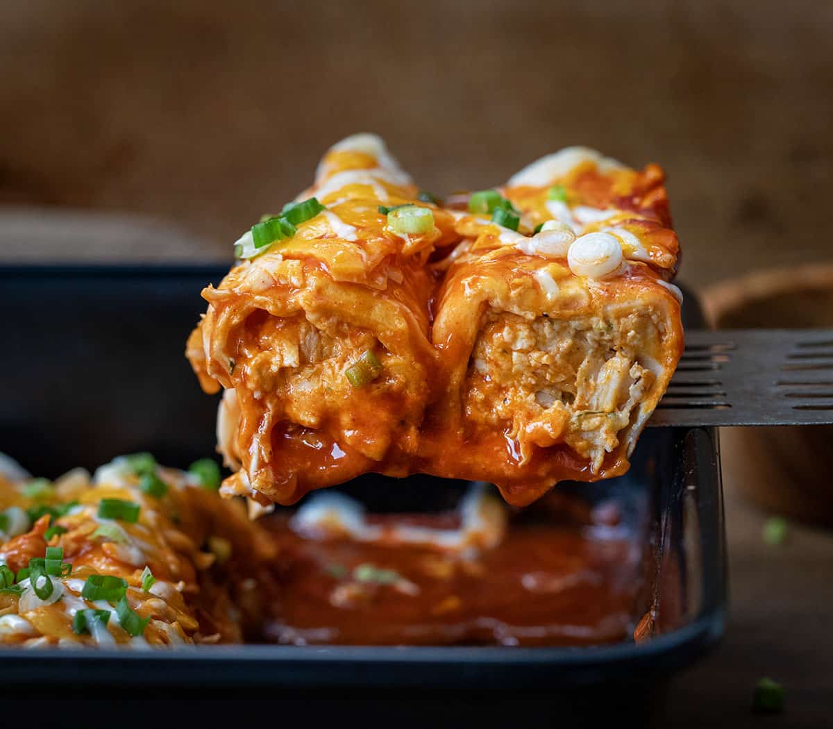 Spatula picking up Buffalo Chicken Enchiladas from the casserole pan.