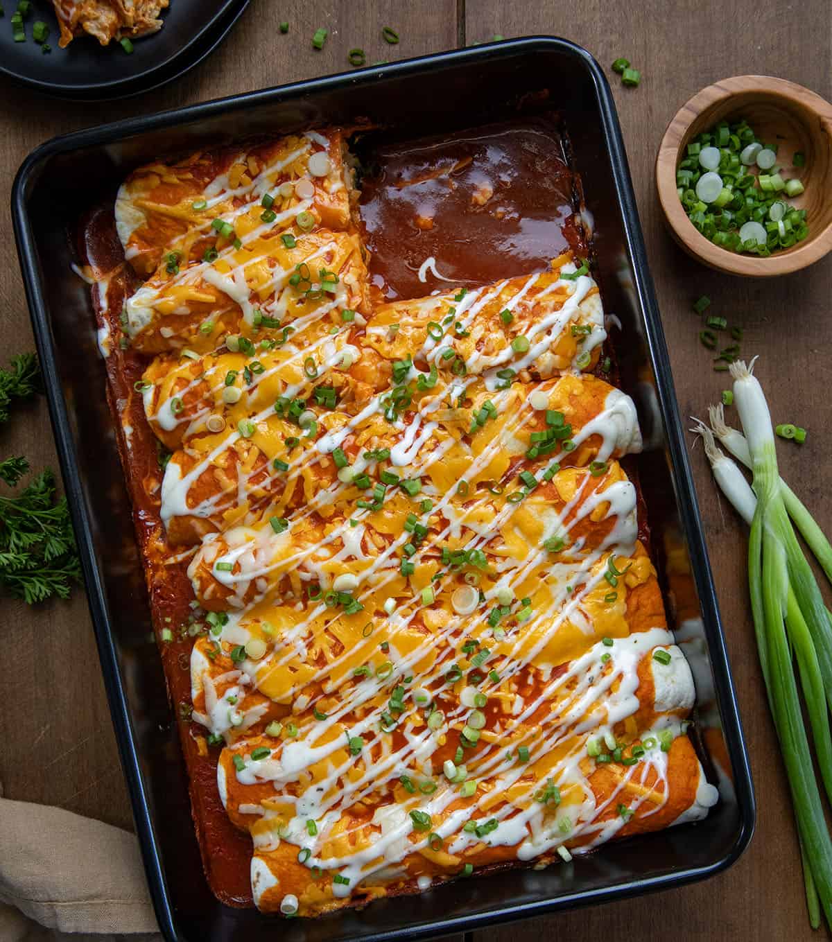 Buffalo Chicken Enchiladas in a dish with two taken out on a wooden table from overhead.